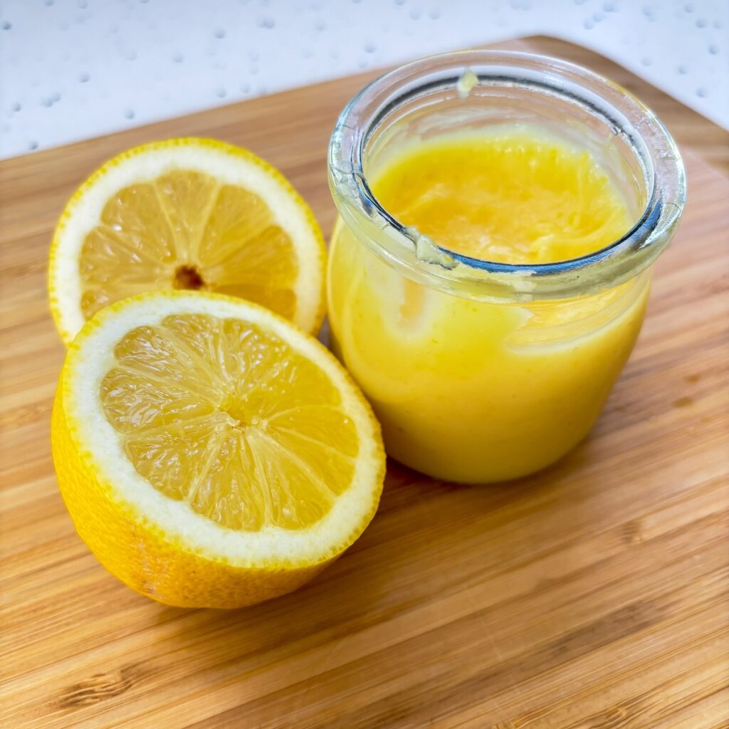Jar of home made lemon curd macaron filling with fresh cut lemons