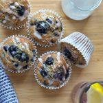 Freshly baked quick and easy Blueberry banana muffins in cases with lemon icing drizzle and refreshing drink