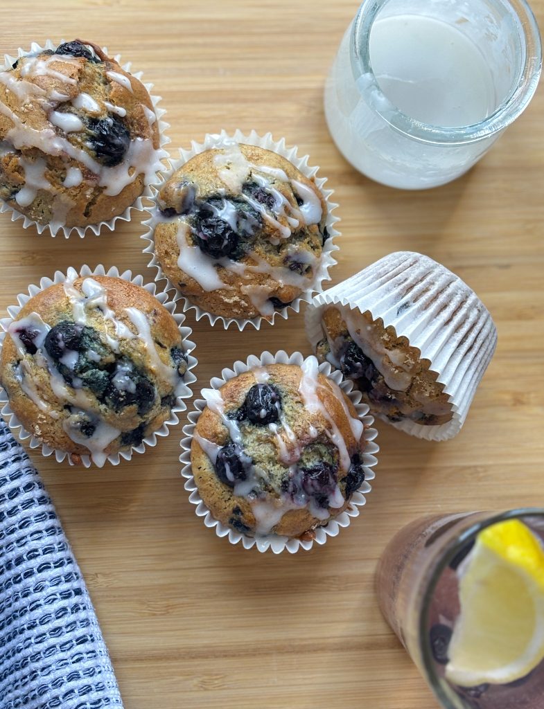 Freshly baked quick and easy Blueberry banana muffins in cases with lemon icing drizzle and refreshing drink