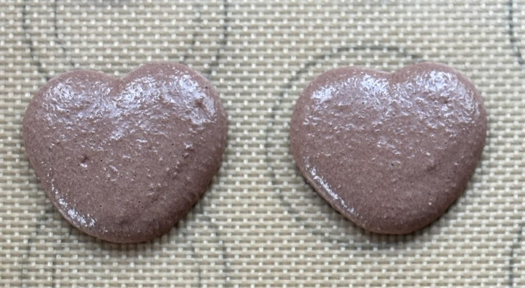 Piped chocolate heart shaped macaron batter on tray