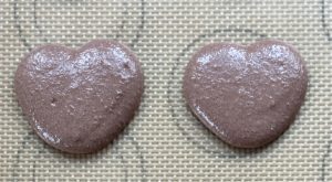 Piped chocolate heart shaped macaron batter on tray