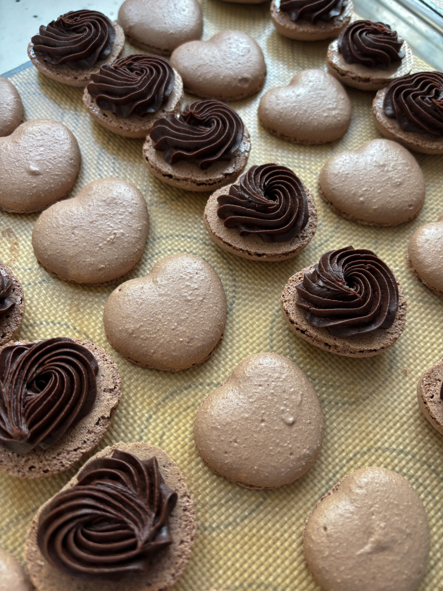 Baked chocolate heart shaped macarons filled with chocolate fudge buttercream for macarons. Macaron filling process picture
