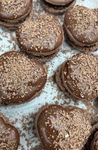 Chocolate macaron hearts dipped in melted chocolate with milk chocolate shavings