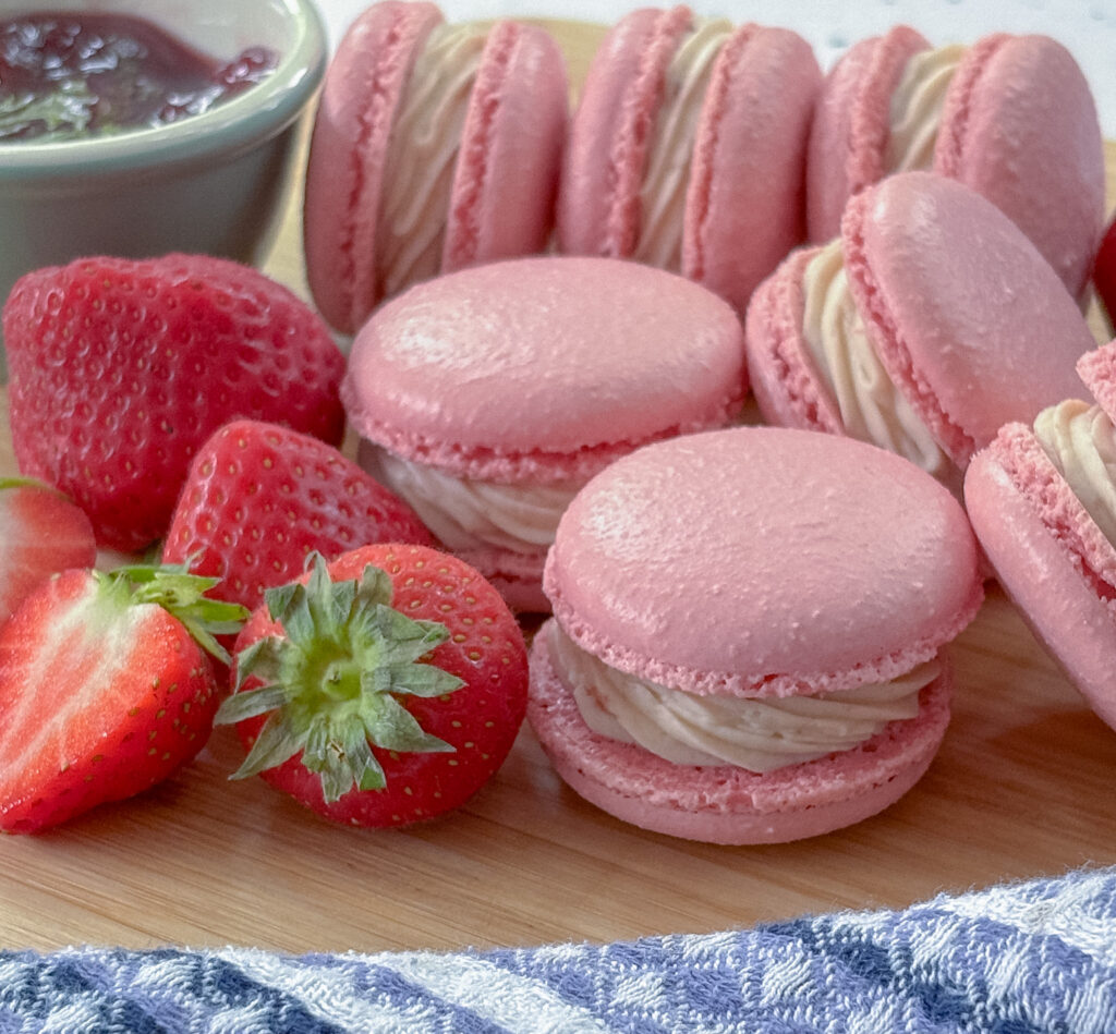 Strawberry macarons with strawberry buttercream filling with fresh strawberries and small bowl of strawberry jam
