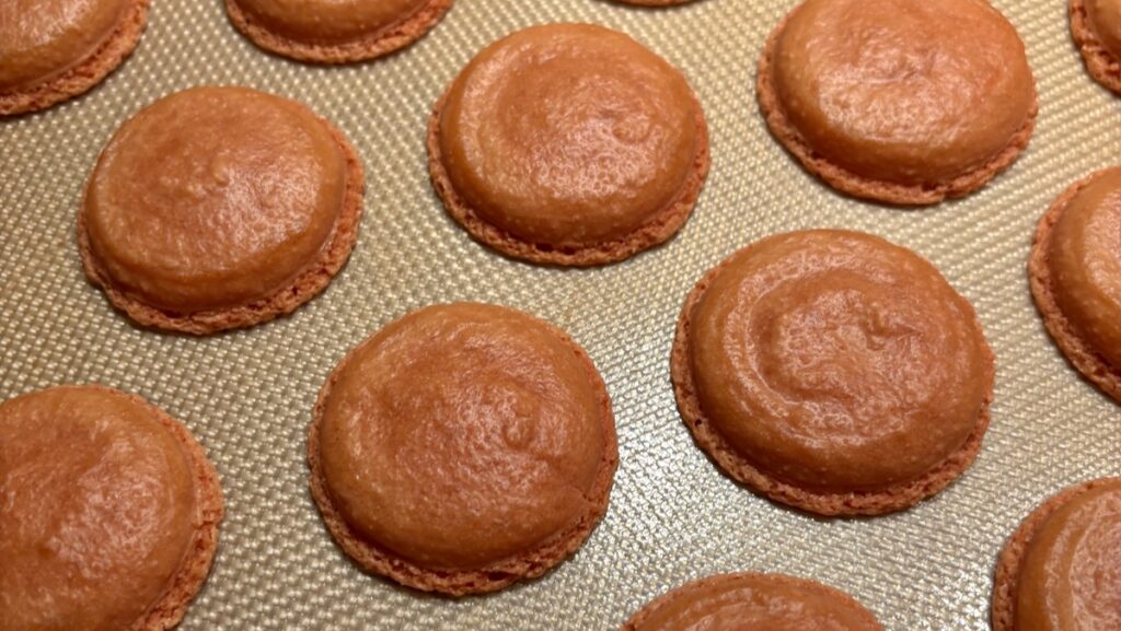 Oily wrinkled wet looking macaron shells on oven tray - oiliness caused by oily almond flour - Macaron Troubleshooting Image