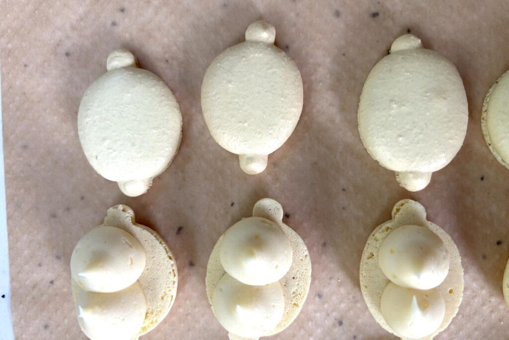 Lemon ganache filling being piped into macaron shell cavity