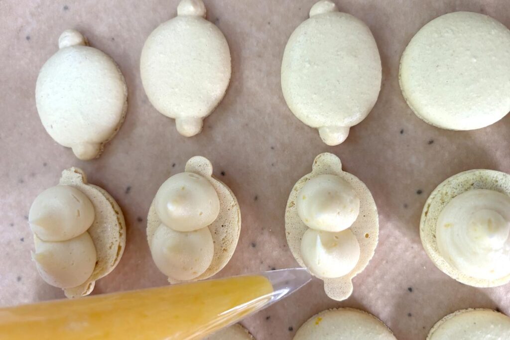 Lemon curd filling being piped into macaron shell cavity
