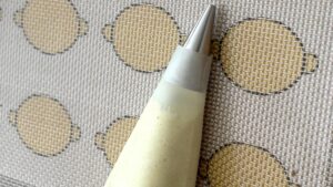 Lemon macaron batter being piped onto parchment paper with a piping bag - Recipe tutorial