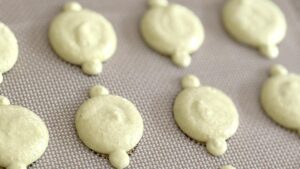 Lemon macaron batter being piped onto parchment paper with a piping bag - Recipe tutorial