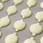 Lemon macaron batter being piped onto parchment paper with a piping bag