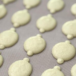 Lemon macaron batter being piped onto parchment paper with a piping bag