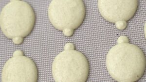 Lemon macaron batter being piped onto parchment paper with a piping bag - Recipe tutorial